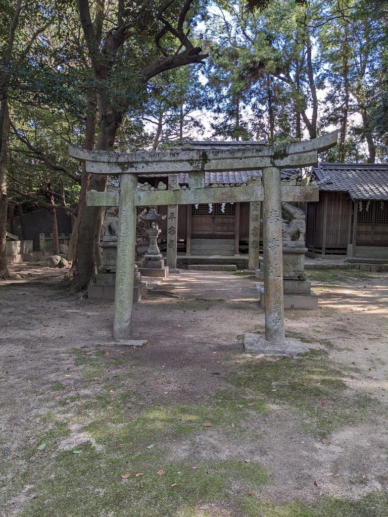 木立の中の石鳥居と、その奥に建つ瓦葺きの社殿