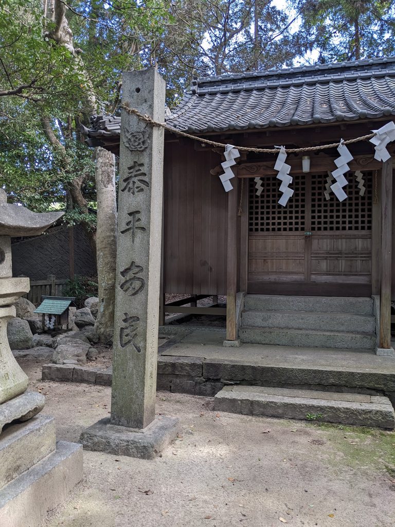 注連縄を掛けた石柱と、その背後に建つ格子戸のある木造社殿