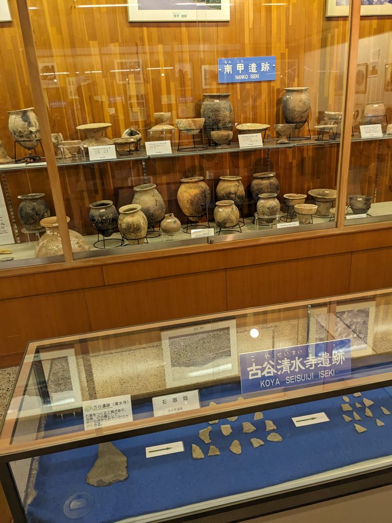 展示ケースに並ぶ土器や石器類と遺跡名の解説札
