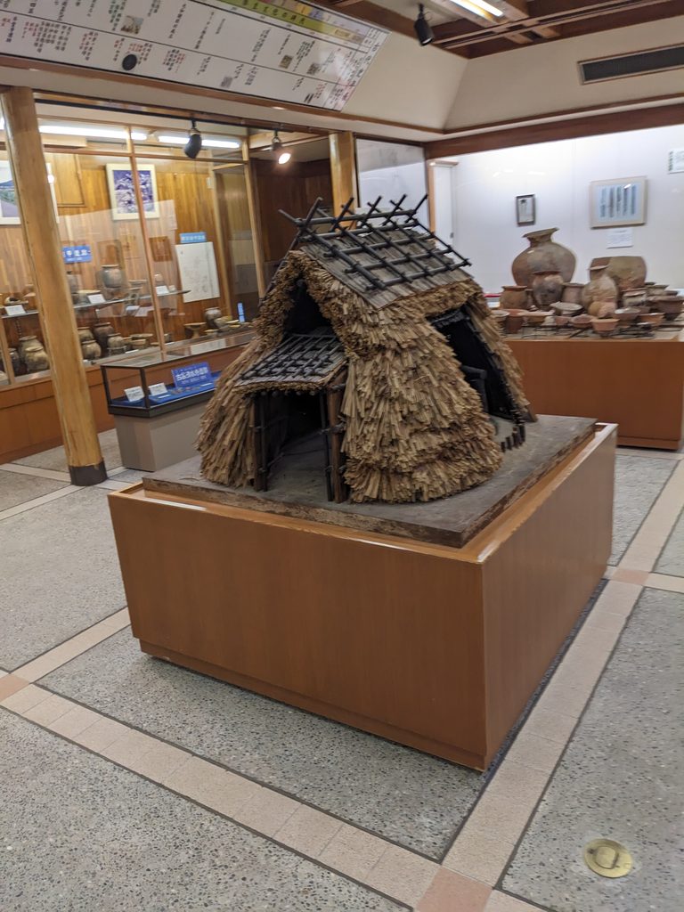展示室に置かれた竪穴住居の復元模型と奥に並ぶ土器